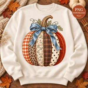 May include: A cream-coloured crewneck sweatshirt featuring a large central graphic of a pumpkin. The pumpkin is divided into vertical segments with patterns including red gingham, leopard print, floral, plaid, and black polka dots, topped with a blue bow.