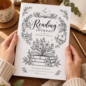 May include: A white reading journal with black line art illustrations of stacked books, flowers, and a teacup. The cover features the text Reading JOURNAL, A little space for every story, and THIS JOURNAL BELONGS TO with a line for a name and year.