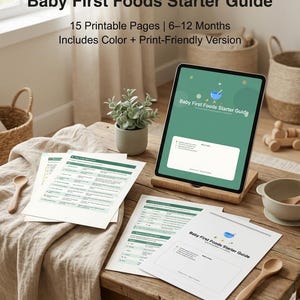 Puede incluir: Una tableta digital y páginas impresas que muestran el texto "Baby First Foods Starter Guide". La tableta está sobre un soporte de madera, y las páginas están sobre una mesa de madera con una planta, cucharas de madera y un cuenco. La guía incluye 15 páginas imprimibles para bebés de 6 a 12 meses.