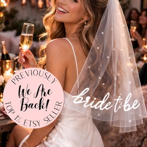 Könnte beinhalten: Eine Braut in spe trägt ein weißes Satinkleid und einen Schleier mit Perlenakzenten. Auf dem Schleier steht "bride to be". Ein rosa Kreis mit dem Text "Previously We Are Back! Top 1% Etsy Seller" ist sichtbar.