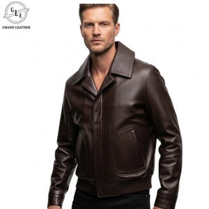 May include: A brown leather jacket with a wide collar and two front pockets. The jacket has a bomber-style design with a ribbed hem and cuffs. The brand logo "GRAND LEATHER" is visible in the upper left corner.