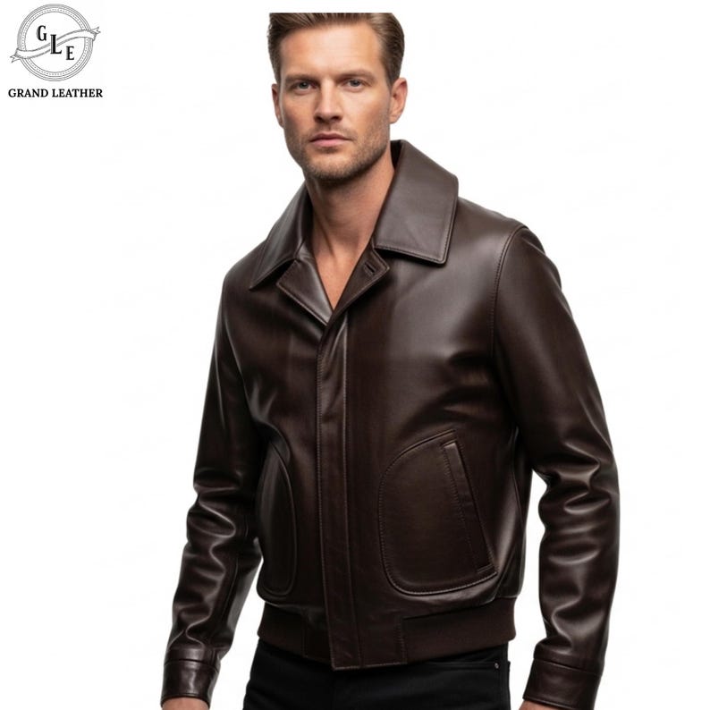 May include: A brown leather jacket with a wide collar and two front pockets. The jacket has a bomber-style design with a ribbed hem and cuffs. The brand logo "GRAND LEATHER" is visible in the upper left corner.