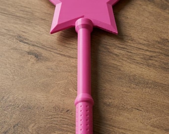 May include: A bright pink star-shaped wand featuring a long, cylindrical handle with a textured, dotted grip section. The star topper is five-pointed with beveled edges, and the entire object is constructed from a solid, uniform pink material.