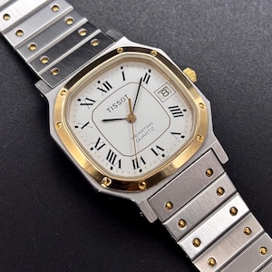 May include: A Tissot Seastar Quartz wristwatch with a white dial, black Roman numeral hour markers, and a date window at the three o'clock position. The watch features a gold-tone octagonal bezel and a two-tone silver and gold-tone metal link band.