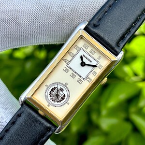 May include: A rectangular wristwatch with a gold-toned frame and a black leather band. The watch face is cream-colored with black numerals and hands. The brand name "YANASE" is visible on the watch face. The watch has a second dial with a crest.