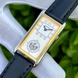 May include: A rectangular wristwatch with a gold-colored frame and a white face. The watch has a black leather band. The face displays the brand name "YANASE" and a circular emblem. The watch measures time with black hands and numerals.