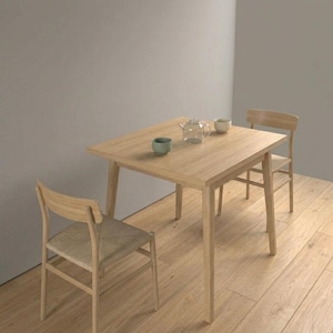 May include: A light wood dining table with two matching chairs. The table has a rectangular top and angled legs. Two small green tea cups, a clear glass teapot, and a white teacup are on the table. The chairs have woven seats.