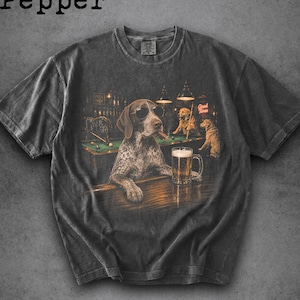 May include: A charcoal grey t-shirt featuring a graphic print of a dog wearing sunglasses and holding a cigar while sitting at a bar with a beer mug. The scene includes other dogs playing billiards in the background and the text Pepper at the top.
