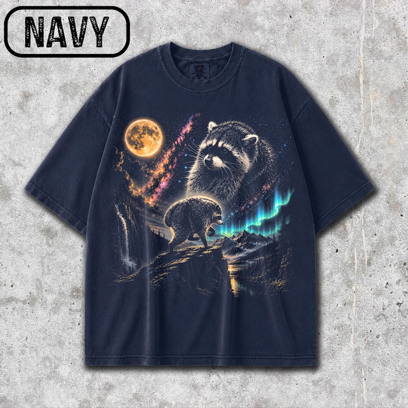 Puede incluir: Una camiseta azul marino de manga corta con un estampado gr&aacute;fico de dos mapaches en un paisaje nocturno. El dise&ntilde;o incluye una luna llena, una nebulosa, una cascada, monta&ntilde;as y auroras boreales. La palabra NAVY est&aacute; impresa en la esquina superior.