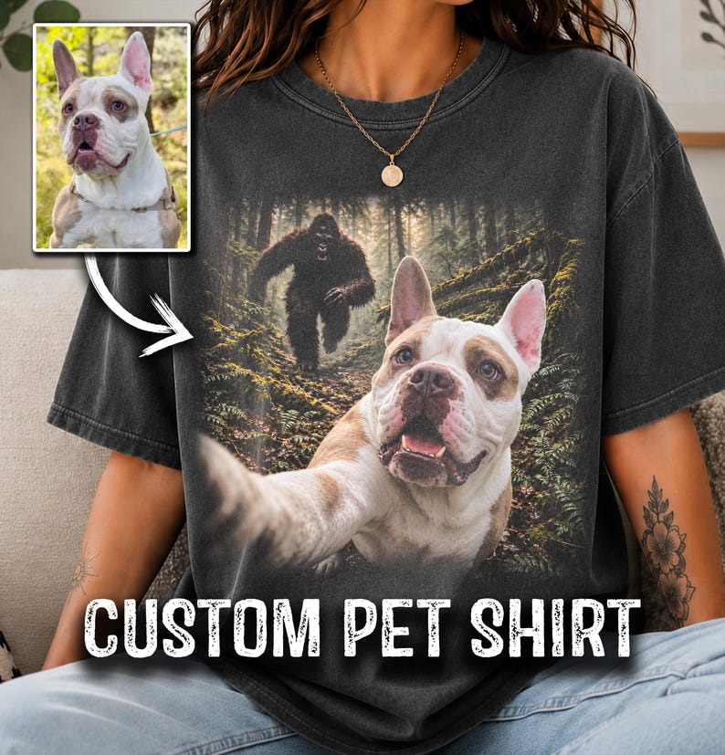 May include: A charcoal grey short-sleeve t-shirt featuring a graphic print of a white and brown dog taking a selfie in a forest with a large dark creature in the background. The shirt includes the text CUSTOM PET SHIRT at the bottom.