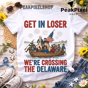 Peut inclure: T-shirt blanc avec le texte "GET IN LOSER" en rouge et bleu, et "WE'RE CROSSING THE DELAWARE" en rouge et bleu. Le t-shirt présente un dessin d'un bateau avec des personnes et un drapeau américain.
