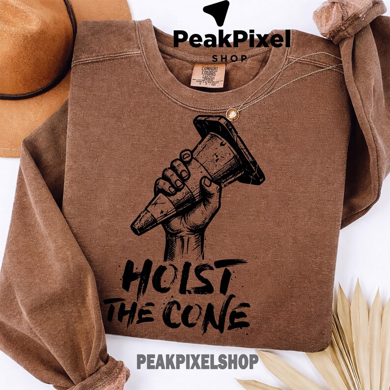 Pu&ograve; includere: Felpa marrone con una grafica nera di una mano che tiene un cono stradale. Il testo "HOIST THE CONE" &egrave; sotto la grafica. La felpa ha un girocollo e maniche lunghe. Il marchio "PeakPixel Shop" &egrave; in alto e in basso.