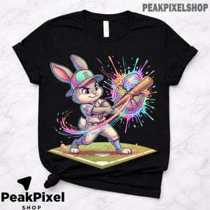 May include: Black t-shirt featuring a cartoon bunny in a baseball uniform, swinging a bat at a colorful, cracked Easter egg. The bunny wears a baseball cap and is on a baseball diamond. The text "PeakPixel Shop" is at the top.