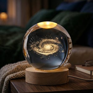May include: A glass sphere lamp featuring a galaxy design, mounted on a round wooden base. The lamp emits a warm, golden light, highlighting the galaxy pattern. The lamp is on a dark wooden bedside table.