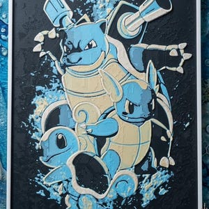 May include: A framed artwork featuring a blue and cream-colored depiction of the Pokémon Blastoise, Wartortle, and Squirtle. The image has a textured appearance with splashes of blue against a black background.