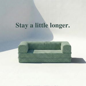 May include: A sage green corduroy sofa with a low-profile, rectangular design. The text "Stay a little longer." is positioned above the sofa, and the text "TUFT x FINCH." is centered below the sofa on a plain white background.