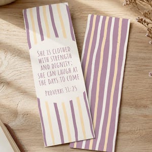 Könnte beinhalten: Zwei rechteckige Lesezeichen mit vertikalen Streifen in Lavendel, Creme und Weiß. Ein Lesezeichen zeigt den Text "SHE IS CLOTHED WITH STRENGTH AND DIGNITY; SHE CAN LAUGH AT THE DAYS TO COME PROVERBS 31:25" in einem weißen rechteckigen Feld.