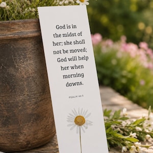 Könnte beinhalten: Ein weißes, rechteckiges Lesezeichen mit dem schwarzen Aufdruck: God is in the midst of her; she shall not be moved; God will help her when morning dawns. PSALM 46:5. Unter dem Text befindet sich eine Illustration einer weißen Margerite mit gelber Mitte.