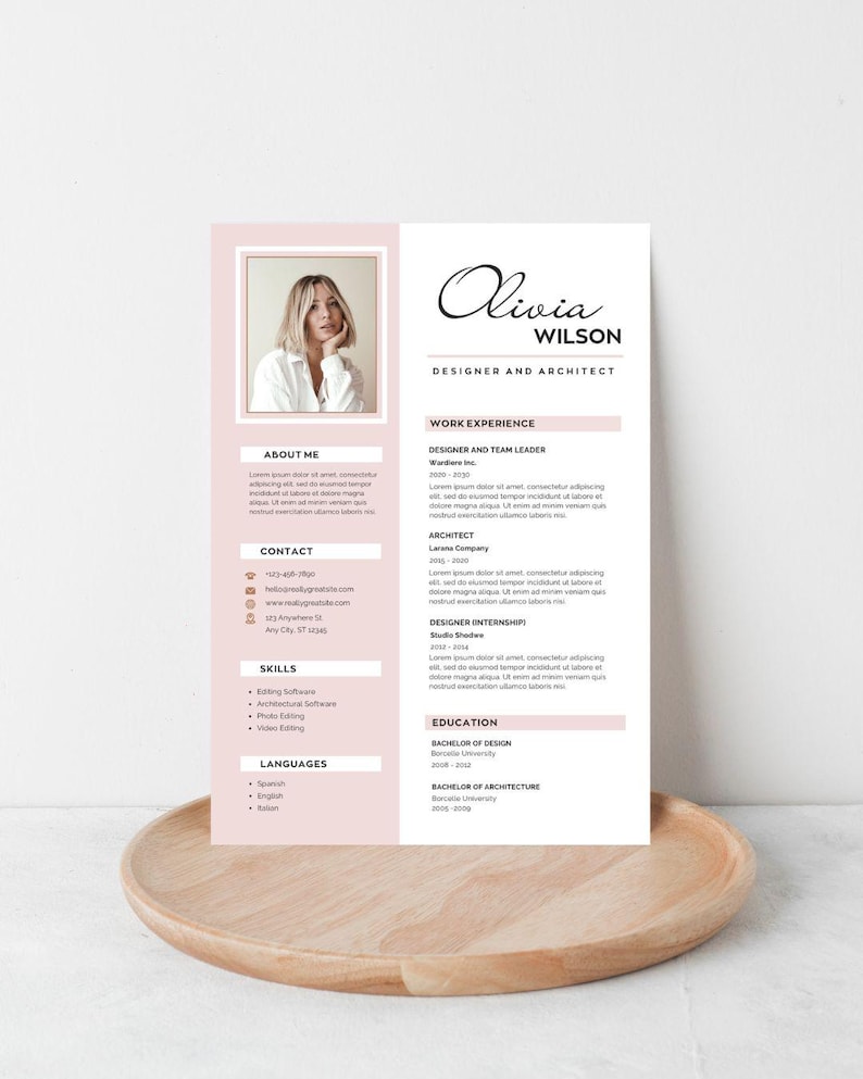 May include: A resume template with a photo, the name "Olivia Wilson", and the title "Designer and Architect". The resume has sections for work experience, skills, and education, with a soft pink color scheme. It is displayed on a wooden tray.