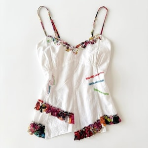 Peut inclure: Débardeur blanc avec bretelles et bordures à imprimé floral. Le haut présente des accents brodés colorés et un ourlet à volants avec un motif floral vibrant. Le design est asymétrique, ajoutant une touche unique au vêtement.