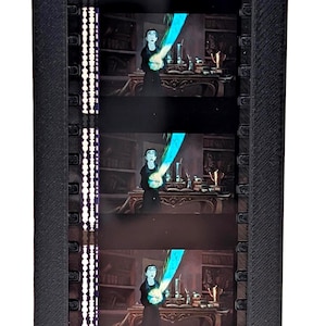 Puede incluir: Una pantalla de tira de pel&iacute;cula negra con cinco fotogramas de una pel&iacute;cula de animaci&oacute;n. Cada fotograma muestra un personaje de negro con un efecto azul brillante. La pantalla tiene un marco negro con una tira de luz vertical.