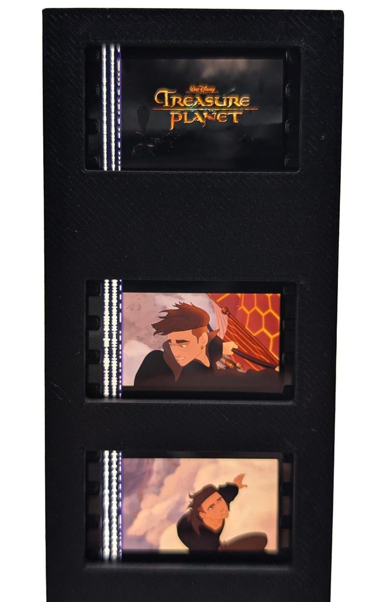 May include: Black film cell display featuring three frames from the animated movie "Treasure Planet." The top frame displays the movie title. The other frames show animated characters in action. The display is black.