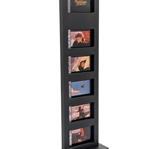 May include: A black display stand featuring six small, rectangular frames. Each frame contains a scene from the animated film "Treasure Planet." The top frame displays the film's title. The stand is made of a textured, dark material.