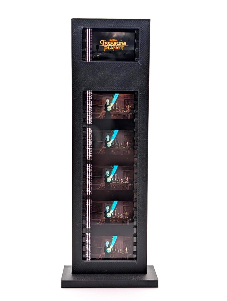 Puede incluir: Exhibidor de tira de pel&iacute;cula negra con el logotipo de "Treasure Planet" en la parte superior. La pantalla muestra varios fotogramas de la pel&iacute;cula. La pantalla es rectangular con una base y un marco negros y un aspecto texturizado.