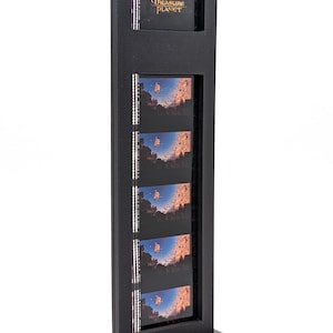 May include: Black display stand featuring film strips with images from "Treasure Planet." The stand has a rectangular frame with a base. The top section displays the movie title. The film strips show a ship sailing in a blue sky.