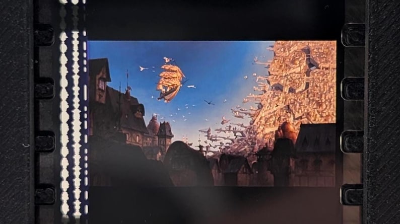 May include: A film strip showing a fantastical scene with a sailing ship floating in the sky above a town. The sky is blue with birds flying. Buildings and structures are on the left and right sides of the image.