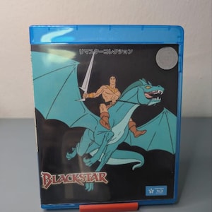 Puede incluir: Una caja azul de Blu-ray con una ilustración de dibujos animados de un guerrero montando un dragón turquesa, sosteniendo una espada. El título "Blackstar" se muestra en una fuente estilizada. También se ve texto japonés.