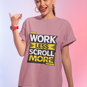 Könnte beinhalten: Staubrosa T-Shirt mit dem Text "WORK LESS SCROLL MORE" in Schwarz und Gelb. Das Shirt hat hochgekrempelte Ärmel. Eine rote Uhr ist am linken Handgelenk zu sehen.