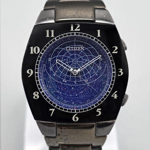 May include: A black Citizen watch with a dark blue face featuring a star map design. The watch has silver hands and hour markers, with a stainless steel band. The watch face displays the word "CITIZEN".
