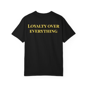 Könnte beinhalten: Schwarzes T-Shirt mit dem Text "LOYALTY OVER EVERYTHING" in gelben Blockbuchstaben. Das kurzärmelige Shirt ist aus einem weichen Material und eignet sich für Freizeitkleidung. Der Text ist auf der Rückseite des Shirts zentriert.