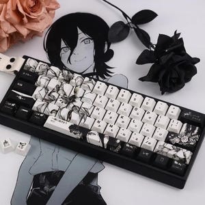 Pode incluir: Teclado mecânico preto com teclas brancas e pretas com ilustrações em estilo anime. O teclado tem uma estrutura preta e inclui caracteres japoneses em algumas teclas. Uma rosa preta e arte de personagens de anime estão no fundo.