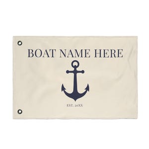 Op de afbeelding: Crèmekleurige nautische vlag met marineblauwe tekst en ankerafbeelding. De tekst luidt "BOAT NAME HERE" boven een marineblauw ankerontwerp. Onder het anker staat "EST. 20XX". De vlag heeft grommets in elke hoek.
