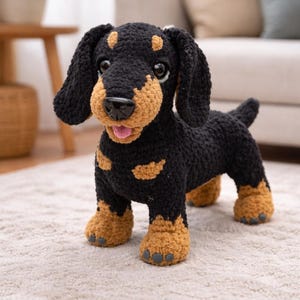 Puede incluir: Un perro salchicha de ganchillo hecho a mano en negro y marrón. El perro tiene orejas caídas y una lengua rosa, de pie sobre una alfombra de color claro. El cuerpo del perro es negro, con detalles marrones en la cara, las patas y el pecho.