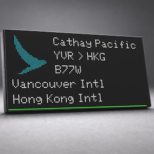 May include: A rectangular black digital display board featuring a teal bird logo and white dot-matrix text that reads Cathay Pacific, YVR > HKG, B77W, Vancouver Intl, and Hong Kong Intl, with a thin green horizontal line at the bottom edge.