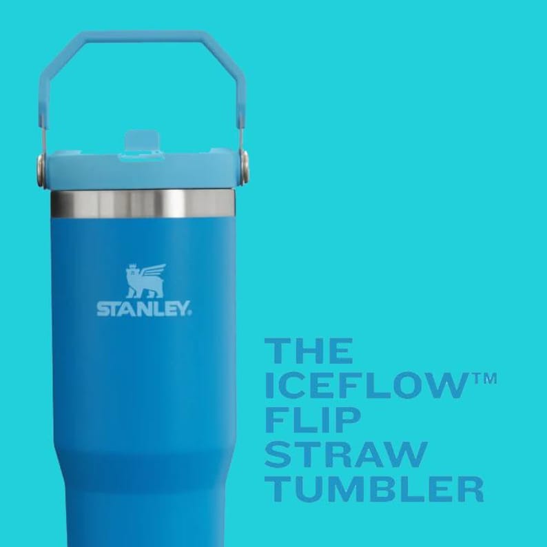 K&ouml;nnte beinhalten: Ein blauer Stanley Iceflow Flip Straw Tumbler mit hellblauem Griff und Deckel. Der Becher hat ein silbernes Band und das Stanley-Logo. Der Text "THE ICEFLOW FLIP STRAW TUMBLER" wird auf der rechten Seite angezeigt.