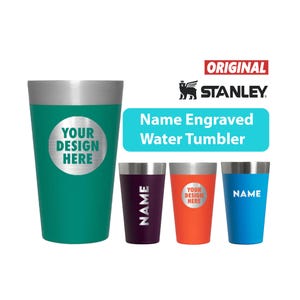 May include: A collection of Stanley water tumblers in various colors, including teal, purple, orange, and blue. Each tumbler has a silver rim and a space for a custom design or name. The text "Name Engraved Water Tumbler" is displayed.