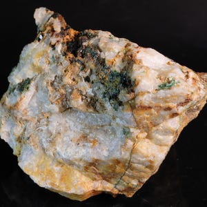 May include: A rough-hewn mineral specimen with a mix of colors. The rock features a base of white and translucent quartz, with patches of green, brown, and orange hues. The surface is textured and uneven, showcasing the natural formation of the stone.
