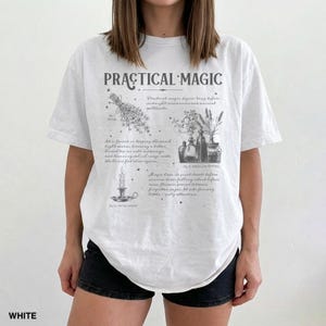 May include: White t-shirt with the text "PRACTICAL MAGIC" and illustrations of herbs, potions, and a candle. The shirt has a relaxed fit and short sleeves. The text "WHITE" is at the bottom left.