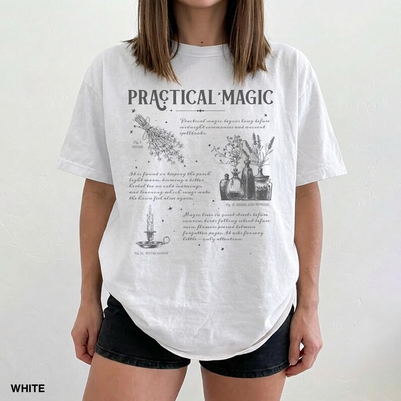 May include: White t-shirt with the text "PRACTICAL MAGIC" and illustrations of herbs, potions, and a candle. The shirt has a relaxed fit and short sleeves. The text "WHITE" is at the bottom left.