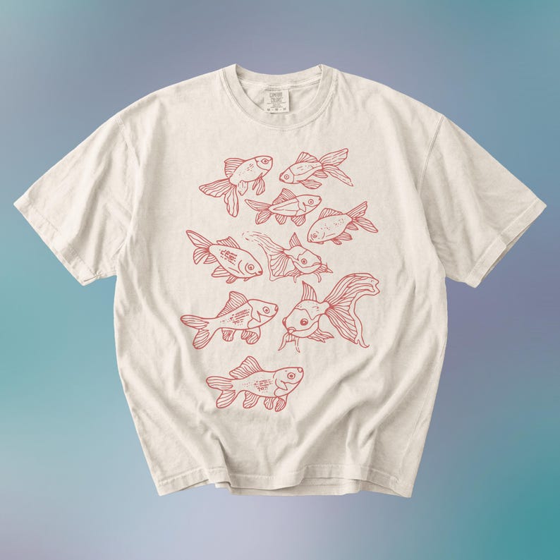 May include: A cream-colored short-sleeve t-shirt featuring a central graphic print of multiple goldfish illustrated in red ink. The design displays various fish in different swimming positions, covering the front center of the garment.