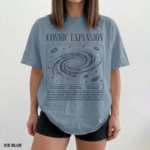 May include: Ice blue t-shirt with a graphic of a galaxy and the words "COSMIC EXPANSION" and "A UNIVERSE IN MOTION". The shirt also has text about the expansion of the universe. The shirt is made of a soft material.