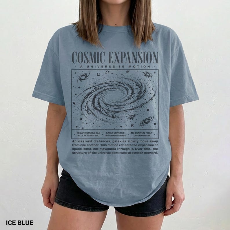 May include: Ice blue t-shirt with a graphic of a galaxy and the words "COSMIC EXPANSION" and "A UNIVERSE IN MOTION". The shirt also has text about the expansion of the universe. The shirt is made of a soft material.