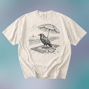 May include: Cream-colored t-shirt featuring a black and white illustration of a raven relaxing on a beach. The raven is under a striped umbrella, with the sun, ocean, and snacks visible. A unique graphic tee.