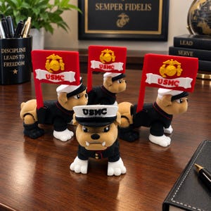 May include: Four bulldog figurines wearing black and white USMC dress uniforms and white caps. Each figure features a red flag with a yellow eagle, globe, and anchor emblem and the text USMC. The bulldogs are standing on a dark wooden surface.