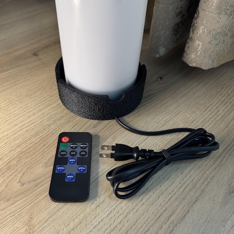 May include: A white cylindrical lamp with a black base, a remote control, and a power cord. The remote has buttons for power, brightness levels, and speed. The lamp is on a wooden surface.