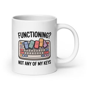 Peut inclure: Mug en céramique blanche avec un design humoristique. Le mug présente le texte "FUNCTIONING?" au-dessus d'un clavier de dessin animé avec des touches colorées, et le texte "NOT ANY OF MY KEYS" en dessous. Les touches du clavier ont des visages.